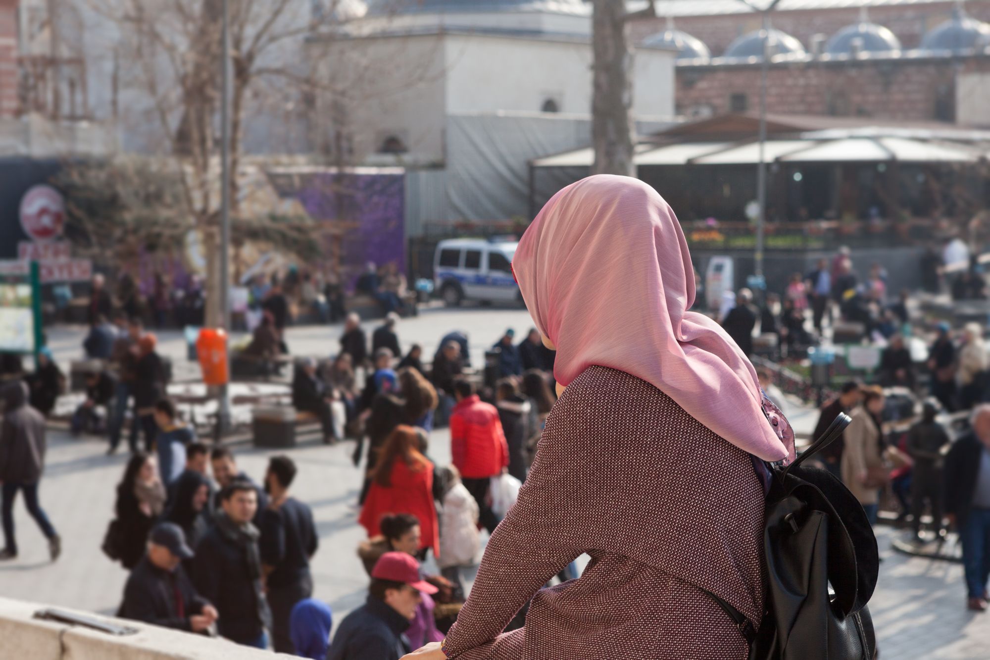Мусульманка сидит на улице, на фоне площадь с людьми.